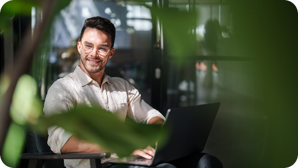 Person working on a laptop behind green leaves